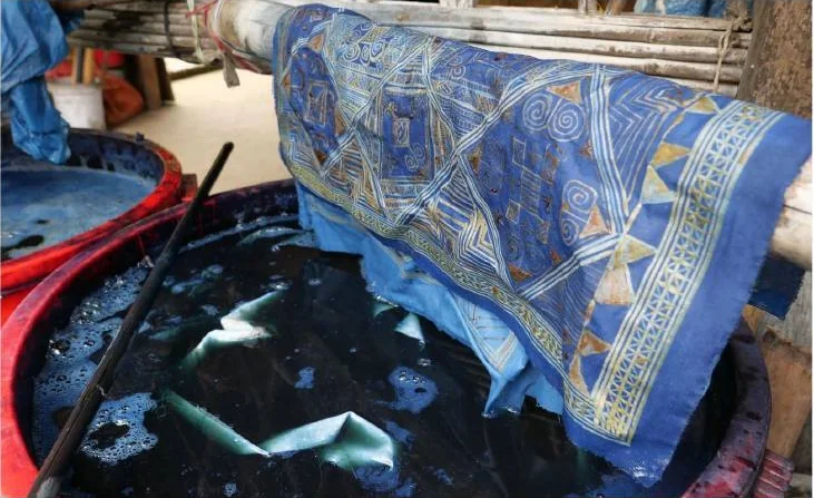 Geometric wax-resist textile suspended above an indigo vat